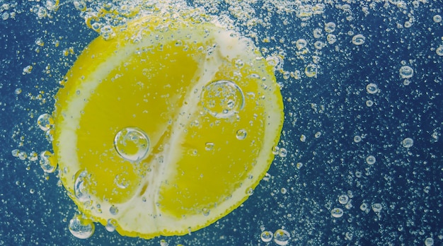 Unterwasser-Zitronenscheibe in Sodawasser oder Limonade mit Blasen. Erfrischender Soda-Tonic-Sprudelcocktail. Nahaufnahme von Zitronen und Eiswürfeln im Glas. Limette in spritzendem Mineralwasser, kaltes Getränk