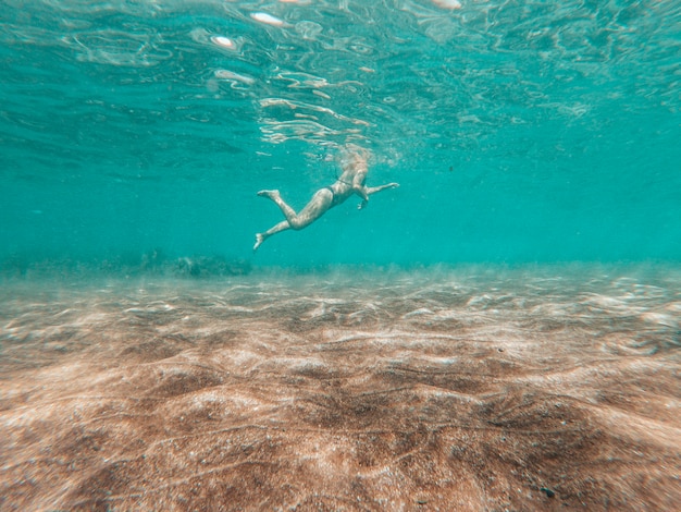 Unterwasseransicht im blauen Meer der aktiven Frau, die den Sommer schwimmt und genießt