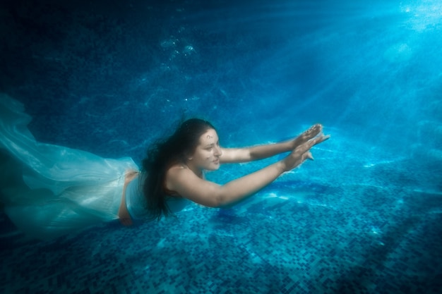 Unterwasseraufnahme einer schönen Frau im Kleid kommt im Lichtstrahl aus dem Pool