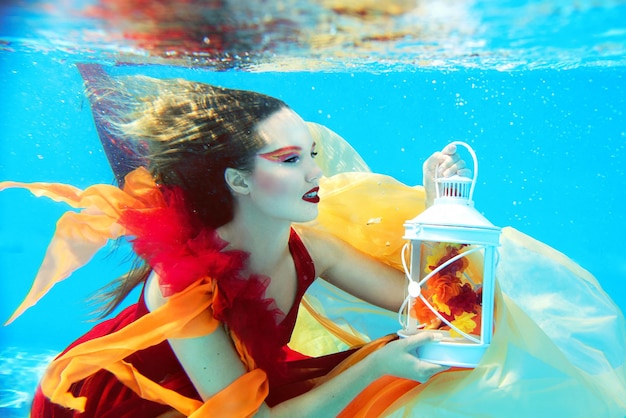 Unterwassermodeporträt der schönen blonden jungen Frau im roten Kleid mit Lampe