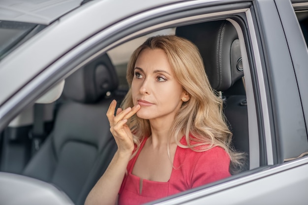 Unterwegs. Hübsche Frau in einem roten Kleid, das in einem Auto sitzt und nachdenklich aussieht