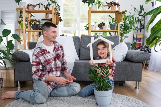 Unvollständige Familie, Vater und Tochter genießen ihr neues Zuhause, sitzen auf dem Sofa, kaufen eine Hypothekenversicherung und ziehen in ihr eigenes Gewächshaus mit Topfpflanze ein und ziehen dort ein