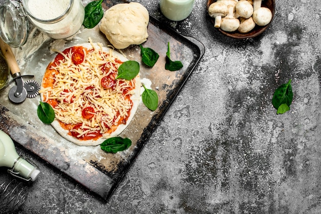 Unvorbereitete Pizza mit Zutaten auf rustikalem Tisch.