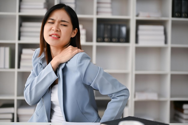 Unwohle asiatische Geschäftsfrau, die bei der Arbeit im Büro unter Schulterschmerzen leidet