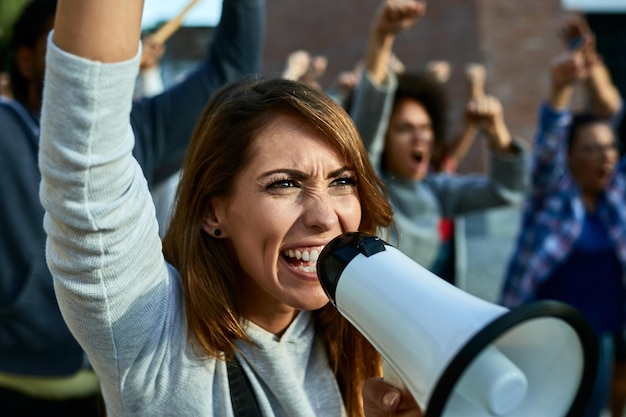 Foto unzufriedene frau, die durch megaphon schreit, während sie mit menschenmassen auf den straßen protestiert