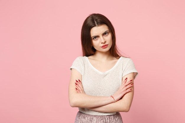 Unzufriedene junge Frau in lässiger leichter Kleidung posiert isoliert auf pastellrosa Wandhintergrund, Studioportrait. Menschen aufrichtige Emotionen Lifestyle-Konzept. Mock-up-Kopienbereich. Halten Sie die Hände gekreuzt.