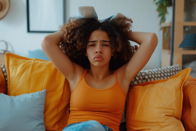 Unzufriedene und wütende lateinamerikanische junge Frau sitzt zu Hause auf dem Sofa und bedeckt die Ohren mit Kissen vor übermäßigem Lärm