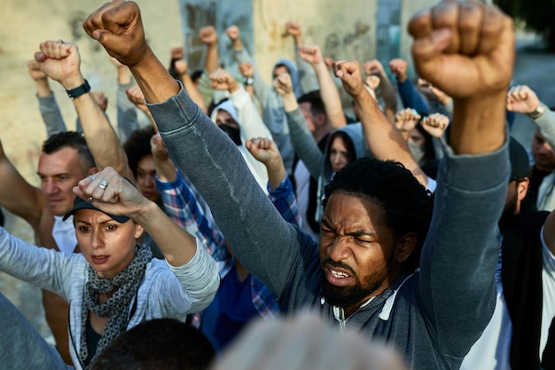 Unzufriedener afroamerikanischer Mann mit erhobenen Fäusten, der mit einer Gruppe von Menschen auf der Straße protestiert