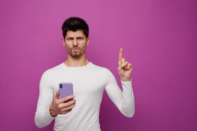 Unzufriedener junger Mann, der das Handy nach oben zeigt, isoliert auf violettem Hintergrund mit Kopierraum