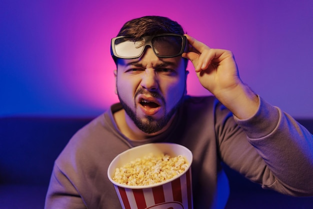 Unzufriedener Mann schaut sich einen Film an, das Gefühl der Wut beim Anschauen eines Films mit Popcorn in hohen Gläsern