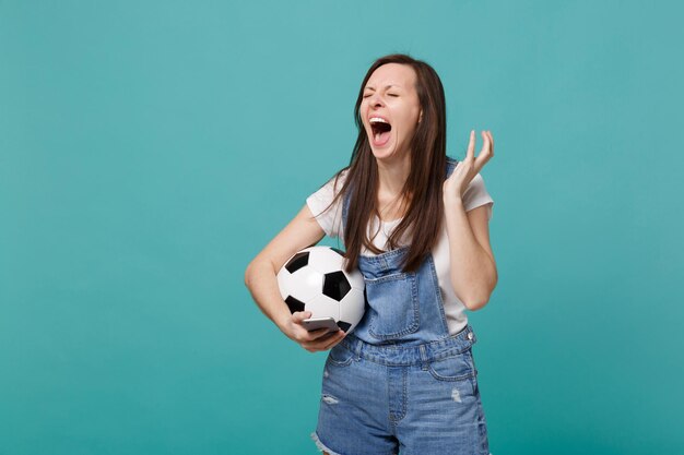 Unzufriedener schreiender Frauenfußballfan mit Fußball mit dem Handy, die Hände einzeln auf blauem türkisfarbenem Hintergrund ausbreitend. Menschen Emotionen, Sport Familienfreizeitkonzept. Kopieren Sie Platz.