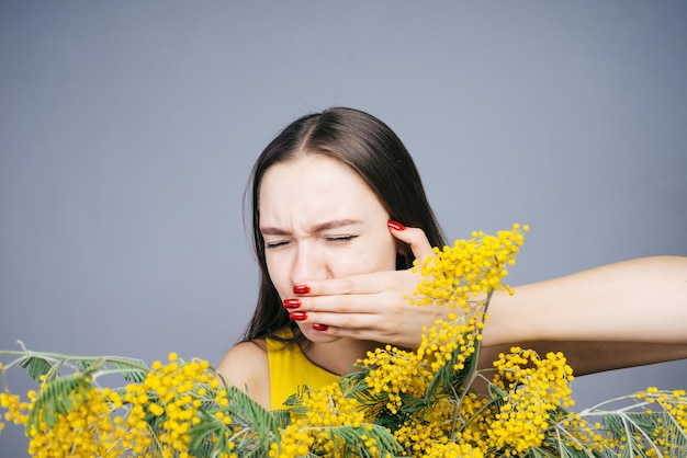 Unzufriedenes junges Mädchen, das einen Strauß aromatischer Mimosen hält, Niesen, allergisch auf Blumen