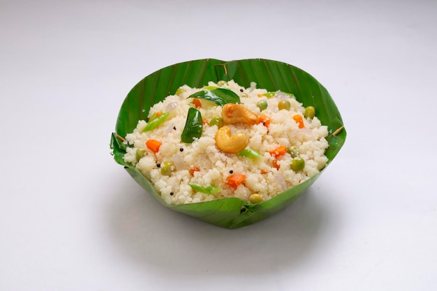 Upma hecho de samolina o rava, artículo de desayuno del sur de la India que está bellamente arreglado en un tazón hecho de hoja de plátano y adornado con anacardos fritos en una servilleta con fondo de textura blanca.