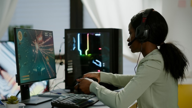 Upsed afrikanische Spielerin, die Online-Videospiele streamt und das Spielen auf einem leistungsstarken RGB-Computer mit einem drahtlosen Controller verliert. Spieler mit Kopfhörern feiert Sieg im Spielzimmer