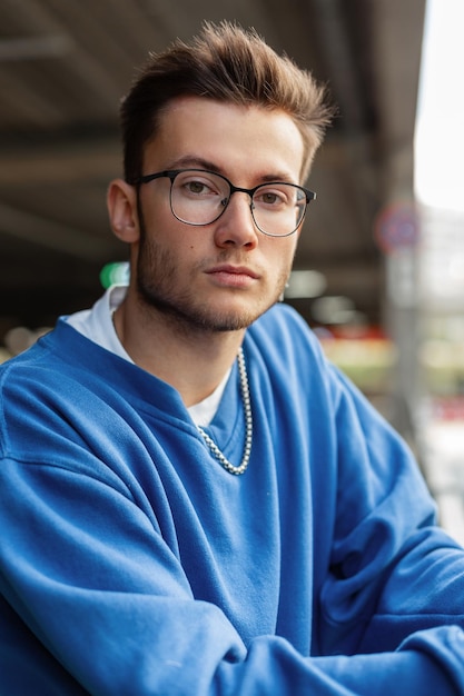 Urban Men's Portrait eines hübschen Hipster-Typen mit Brille in einem modischen blauen Pullover in der Stadt