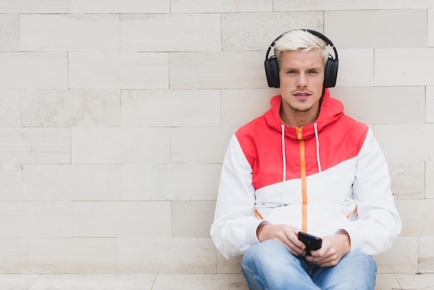 Urban Portrait von attraktiven Männern in roter Sportbekleidung entspannen und sitzen nach körperlichen Aktivitäten im Freien im Park Junger gutaussehender Mann lächelt und hört Musik mit Kopfhörern im Freien