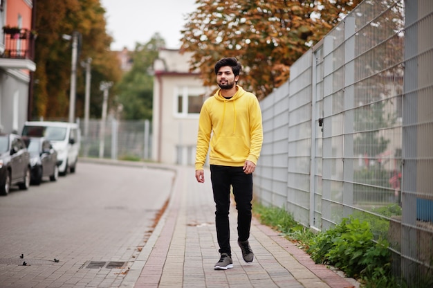 Urbaner junger Hipster-Indianer in einem modischen gelben Sweatshirt. Coole südasiatische Kerl tragen Hoodie, der auf Fallstraße geht.