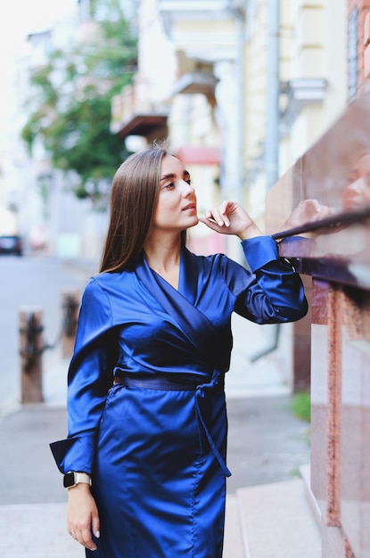 Urbanes Modeporträt einer stilvollen jungen Geschäftsfrau in einem langen blauen Kleid und langen dunklen Haaren.