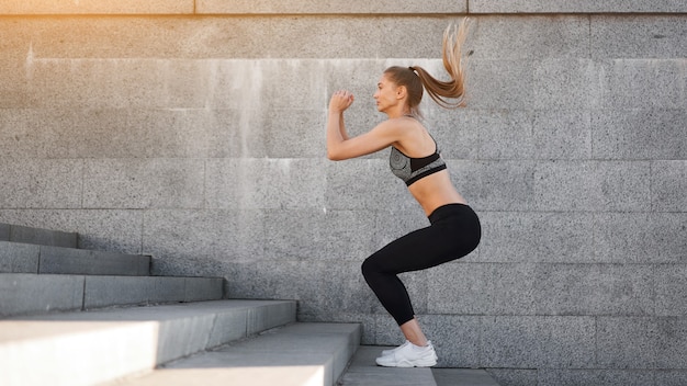 Urbanes sportliches Frauentraining. Sportlerin macht Kniebeugensprünge auf städtischen Treppen.