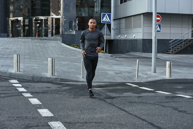 Urbanes Training in voller Länge Porträt eines athletischen afrikanischen Mannes in Sportbekleidung, der auf der Straße läuft