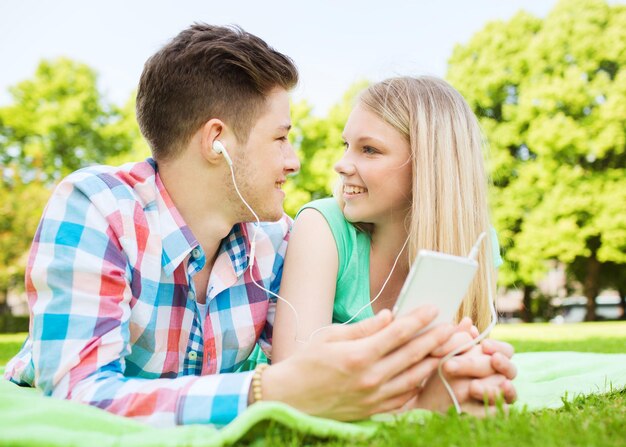 urlaub, ferien, technologie und freundschaftskonzept - lächelndes paar, das auf decke liegt und selfie mit smartphone im park macht