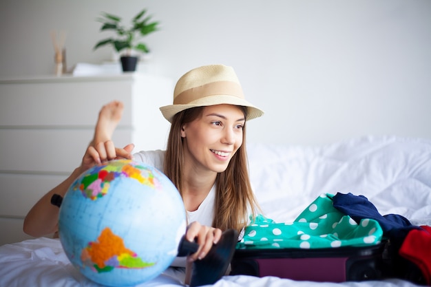 Urlaub. Frau, die für Rest sich vorbereitet. Junges schönes Mädchen sitzt auf dem Bett. Porträt einer lächelnden Frau. Happy Girl geht in den Urlaub