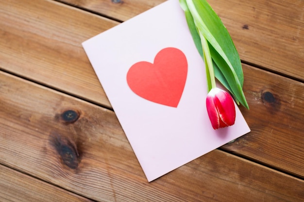 Urlaub, Liebe und Valentinstag Konzept - Nahaufnahme von Tulpenblumen und Grußkarte mit Herz auf Holztisch
