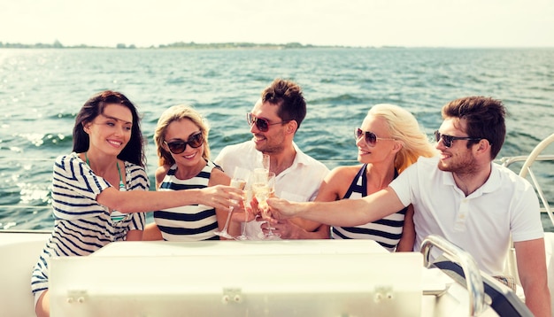 urlaub, reise, meer, freundschaft und personenkonzept - lächelnde freunde mit gläsern champagner auf yacht