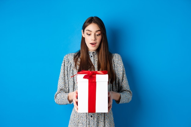 Urlaub überraschte junge frau, die geschenk mit erstauntem gesicht betrachtet, erhalten valentinstag geschenkstand...