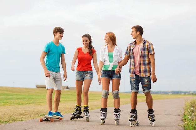 Urlaub, Urlaub, Liebe und Freundschaftskonzept - Gruppe lächelnder Teenager mit Rollschuhen und Skateboardfahren im Freien