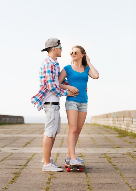 Urlaub, Urlaub, Liebe und Freundschaftskonzept - lächelndes Paar mit Skateboard im Freien