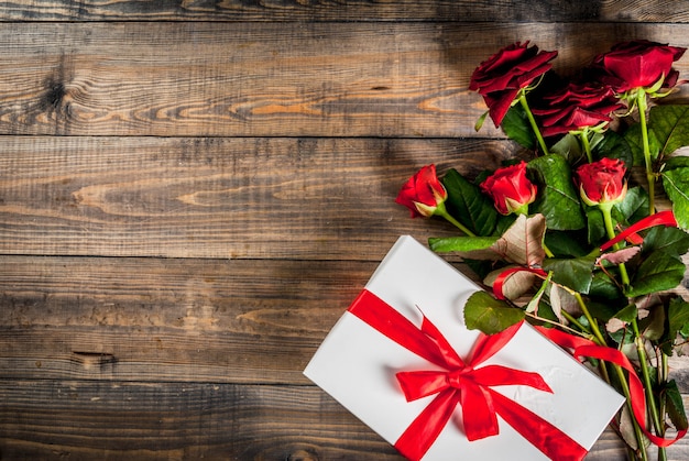 Urlaub, Valentinstag. Strauß roter Rosen, Krawatte mit roter Schleife, mit Geschenkverpackung. Auf Holztisch Draufsicht