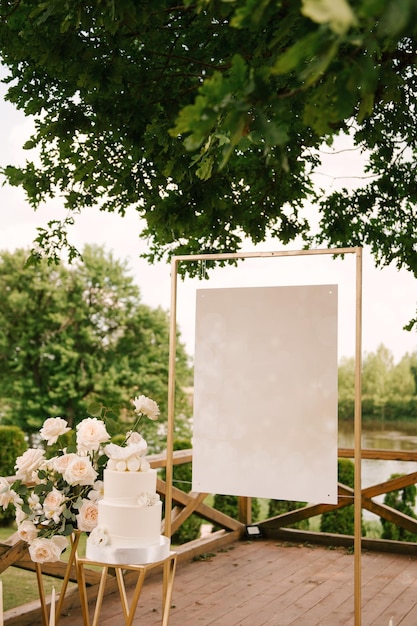 Urlaubs- oder Hochzeitsdekor mit schönen Kompositionen aus weißen Rosen mit leerem Hintergrund und einem weißen Kuchen in der Natur