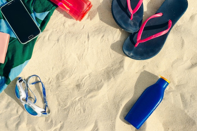 Urlaubs- und Sommerferienkonzept Flip Flops Handtuchkappe Wasserflaschen und Flasche Sonnenschutzöl auf Strandsand