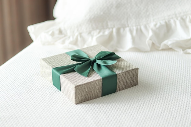 Urlaubsgeschenk und Luxus-Online-Shopping-Lieferung verpackte Leinen-Geschenkbox mit grünem Band auf dem Bett im schicken Landhausstil des Schlafzimmers