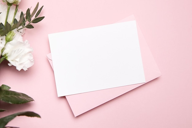 Urlaubsgrußkarte Mockup mit Umschlag und weißen Blumen auf rosafarbenem Hintergrund Draufsicht flach gelegt Leere Hochzeitseinladungskarte Mockup und Blumendekor