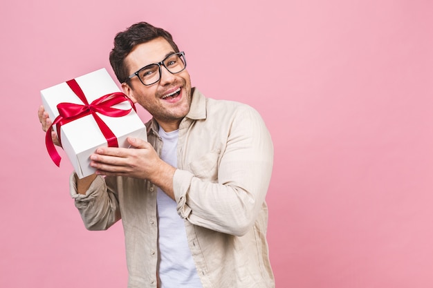 Urlaubskonzept. Porträt eines jungen Mannes, der Geschenkbox lokalisiert über rosa Wand öffnet.