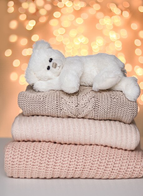 Urso de peluche pequeno branco bonito que encontra-se pacificamente na pilha de camisetas feitas malha.
