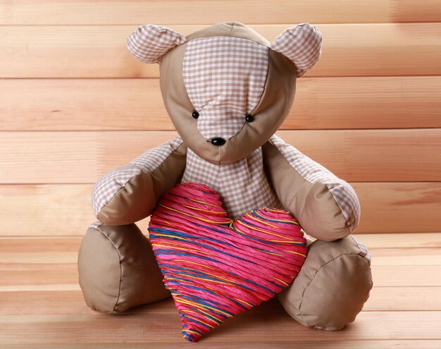 Urso de pelúcia com coração vermelho sobre fundo de madeira