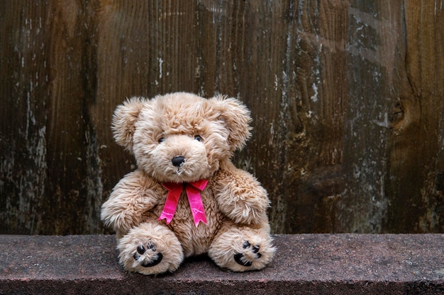 Urso de pelúcia com laço rosa senta-se ao ar livre no fundo de madeira