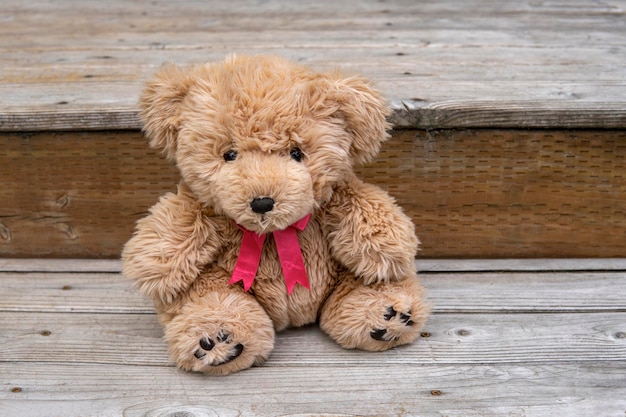 Urso de pelúcia com laço rosa senta-se na varanda de madeira