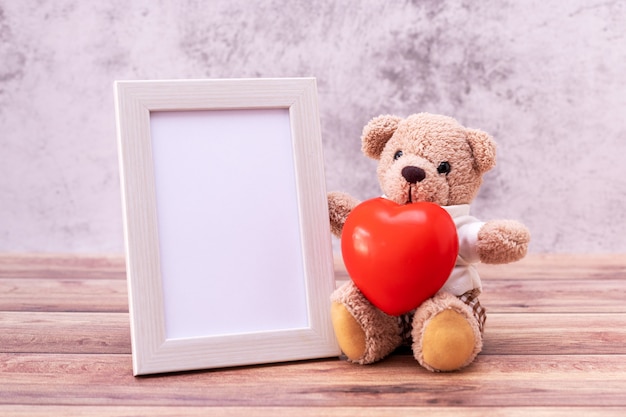 Urso de pelúcia com moldura e coração na mesa