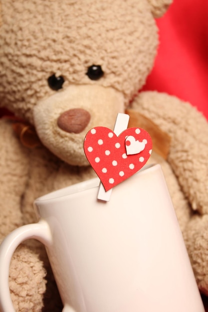Urso de pelúcia com uma grande xícara branca de chá e um coração vermelho