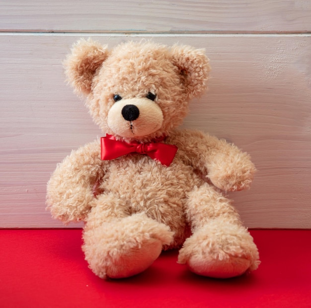 Urso de pelúcia com uma gravata borboleta vermelha sentado no chão vermelho dia dos namorados