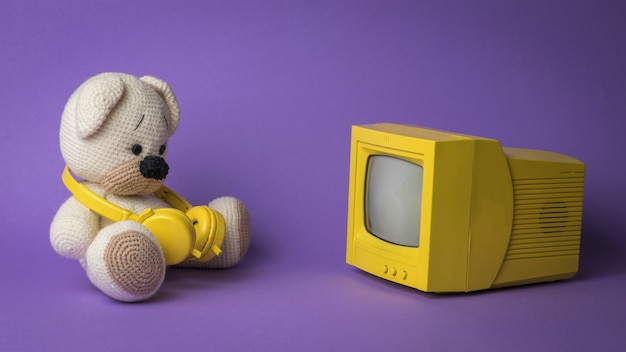 Foto urso de pelúcia de malha com fones de ouvido na frente da tela do monitor.