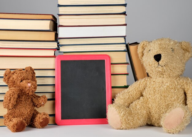 Urso de pelúcia e placa preta vazia no quadro vermelho na pilha de livros