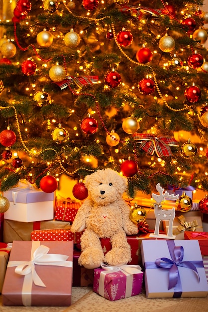 Urso de pelúcia fofo sentado em caixas de presentes sob a linda árvore de natal decorada