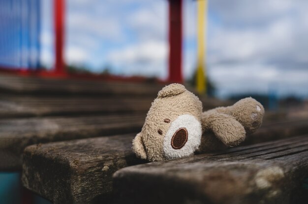 Urso de pelúcia perdido deitado na ponte de madeira no parquinho em um dia sombrio