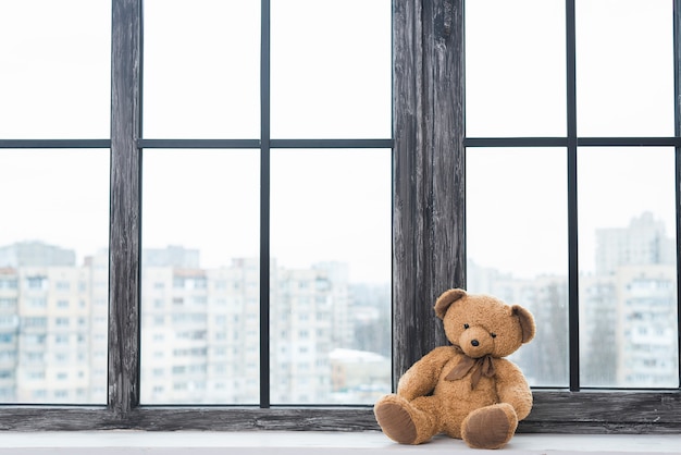 Foto urso de pelúcia solitário sentado perto do peitoril da janela fechada