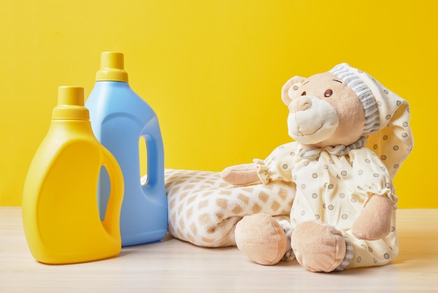 Foto ursos de pelúcia e garrafas com gel de lavagem em um fundo amarelo lavando roupas de bebê conceito